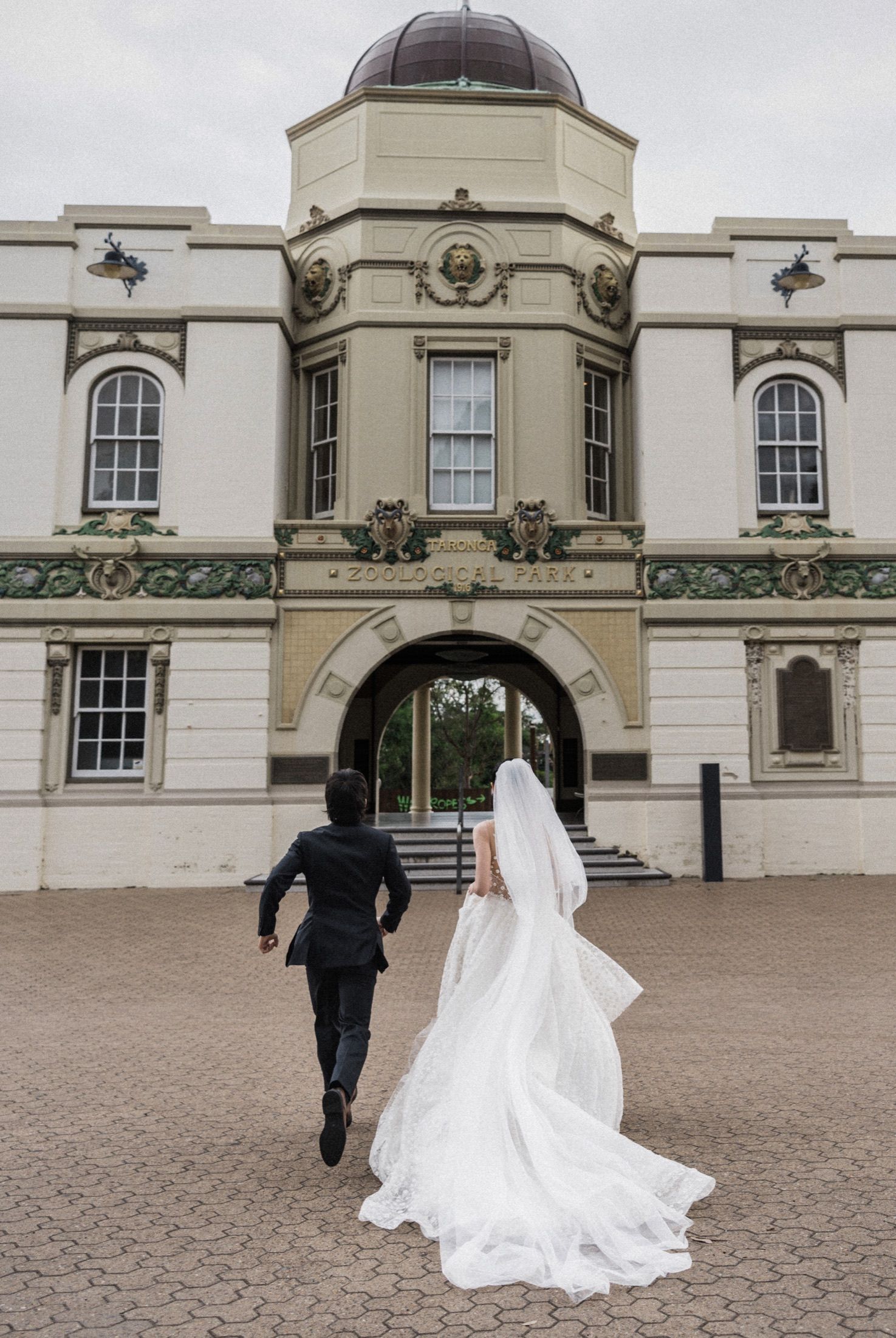 Bride and groom walking hand in hand toward an elegant historic building with ornate architecture on their wedding day.