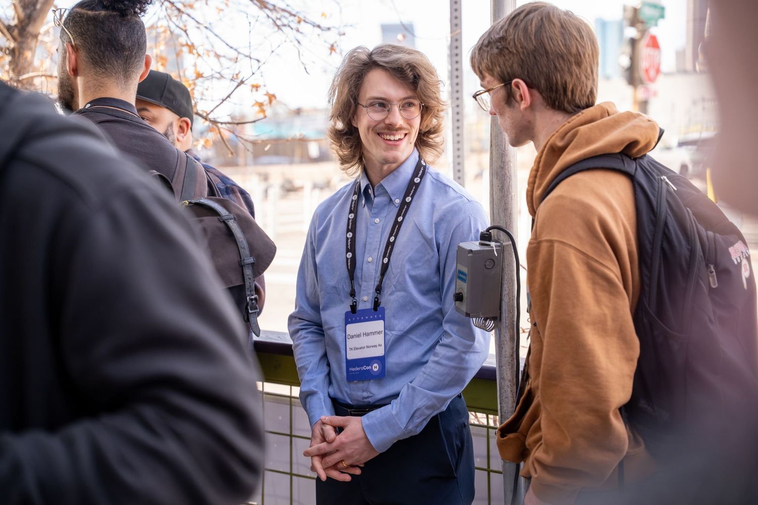 Young man wearing a conference badge smiles while networking with peers outdoors at a professional event.