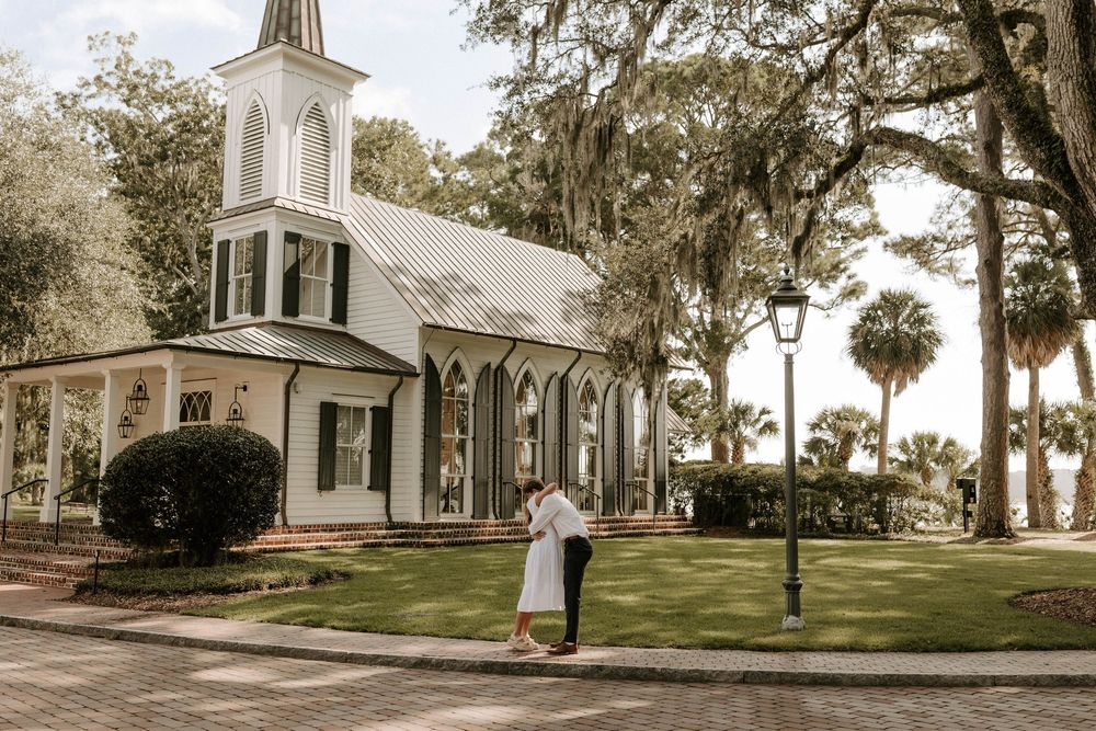 Couple sharing a romantic kiss outside a white chapel with Spanish moss trees in a Southern wedding setting.