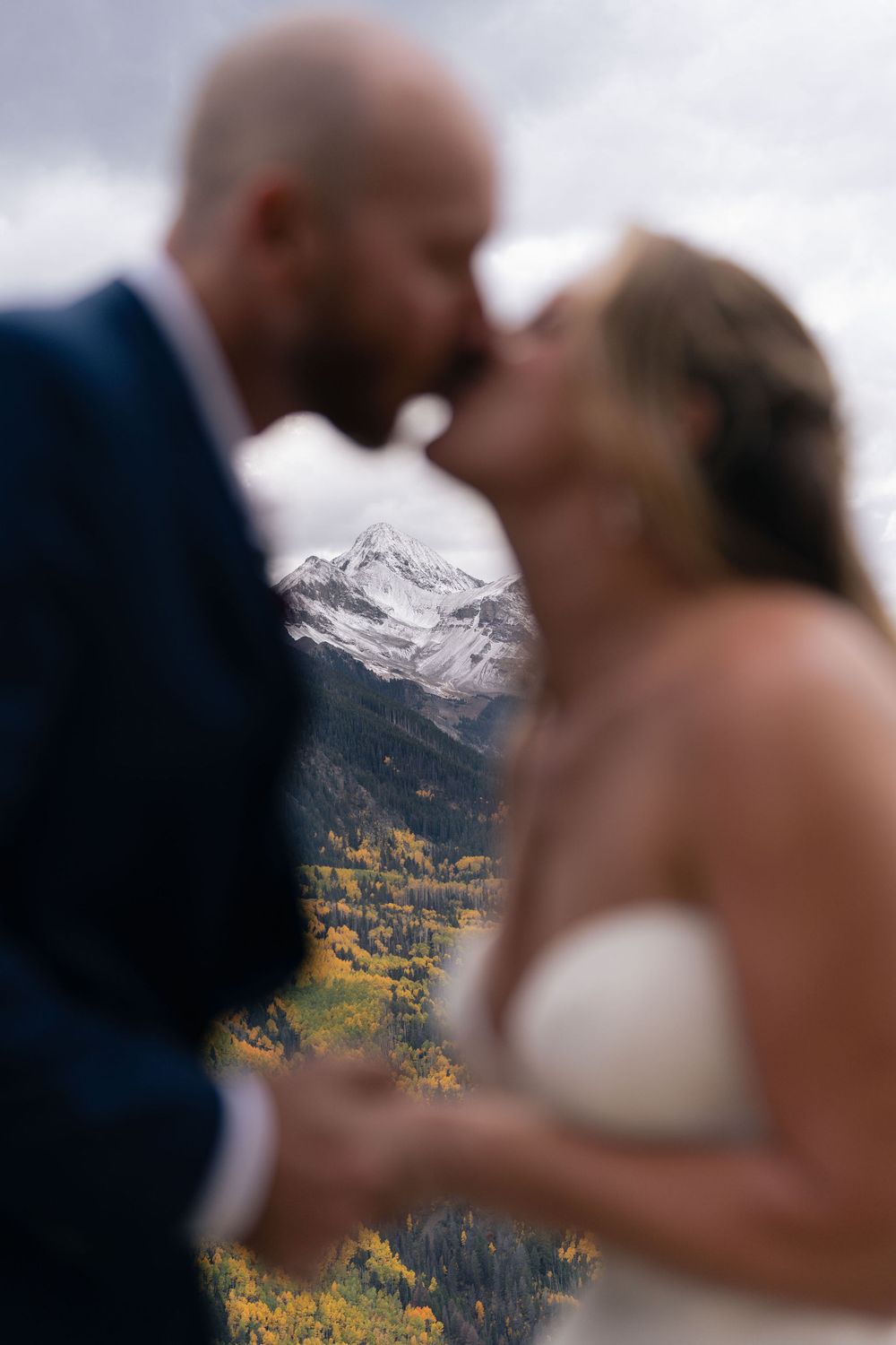 Bride and groom kissing with a snow capped mountain peak behind them at a wedding in Telluride, CO
