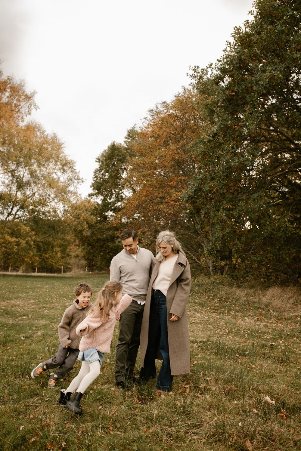 Family of four enjoying an autumn outdoor walk, with parents watching two young children play in a grassy field.