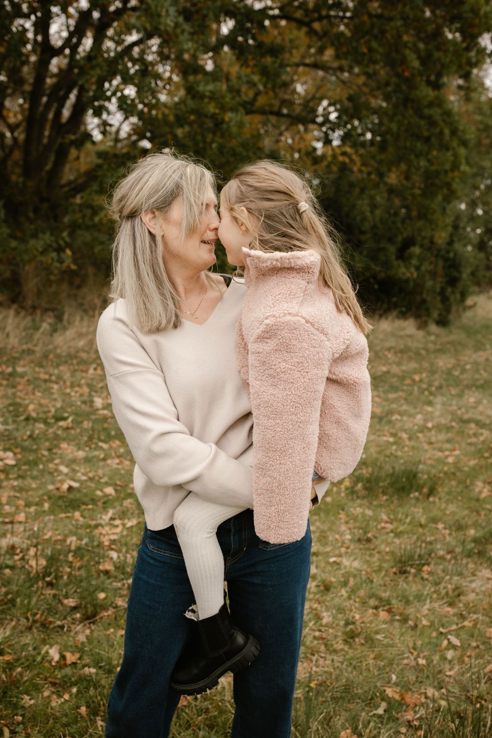 Grandmother tenderly touching foreheads with young granddaughter in autumn park.