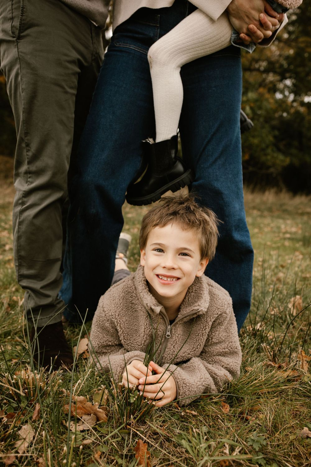 Smiling boy in teddy fleece jacket lying on grass during autumn family photo session outdoors.
