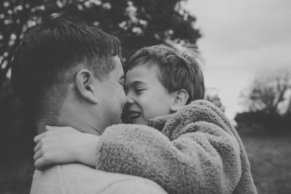 Black and white photo of a father holding and smiling with his young child outdoors.