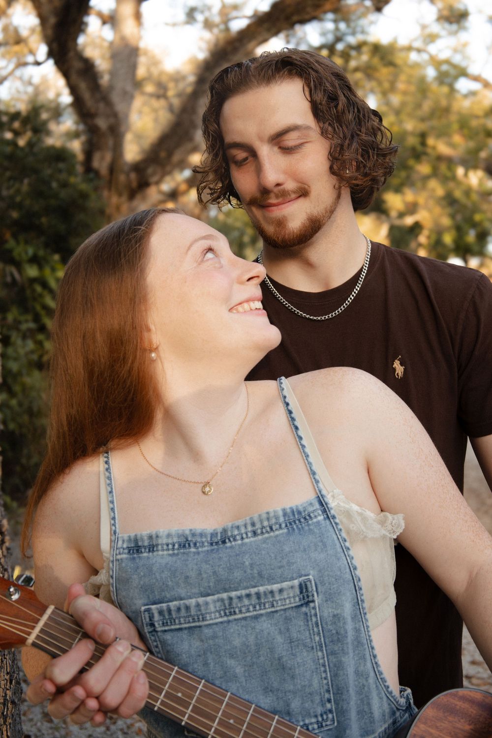 Smiling young couple with a guitar sharing a romantic moment outdoors in warm sunlight.