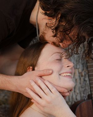 A young couple sharing a tender moment, man gently cupping smiling woman's face outdoors.