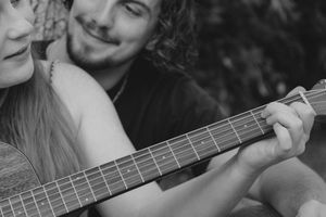 A couple sharing a romantic moment as man plays acoustic guitar in black and white photo.