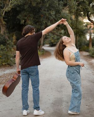 A couple dancing outdoors as man twirls woman while holding an acoustic guitar.