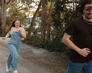 A joyful couple playfully running together on a scenic tree-lined dirt path.