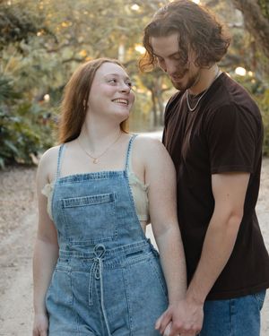 A happy young couple holding hands and smiling at each other on a sunlit garden path.