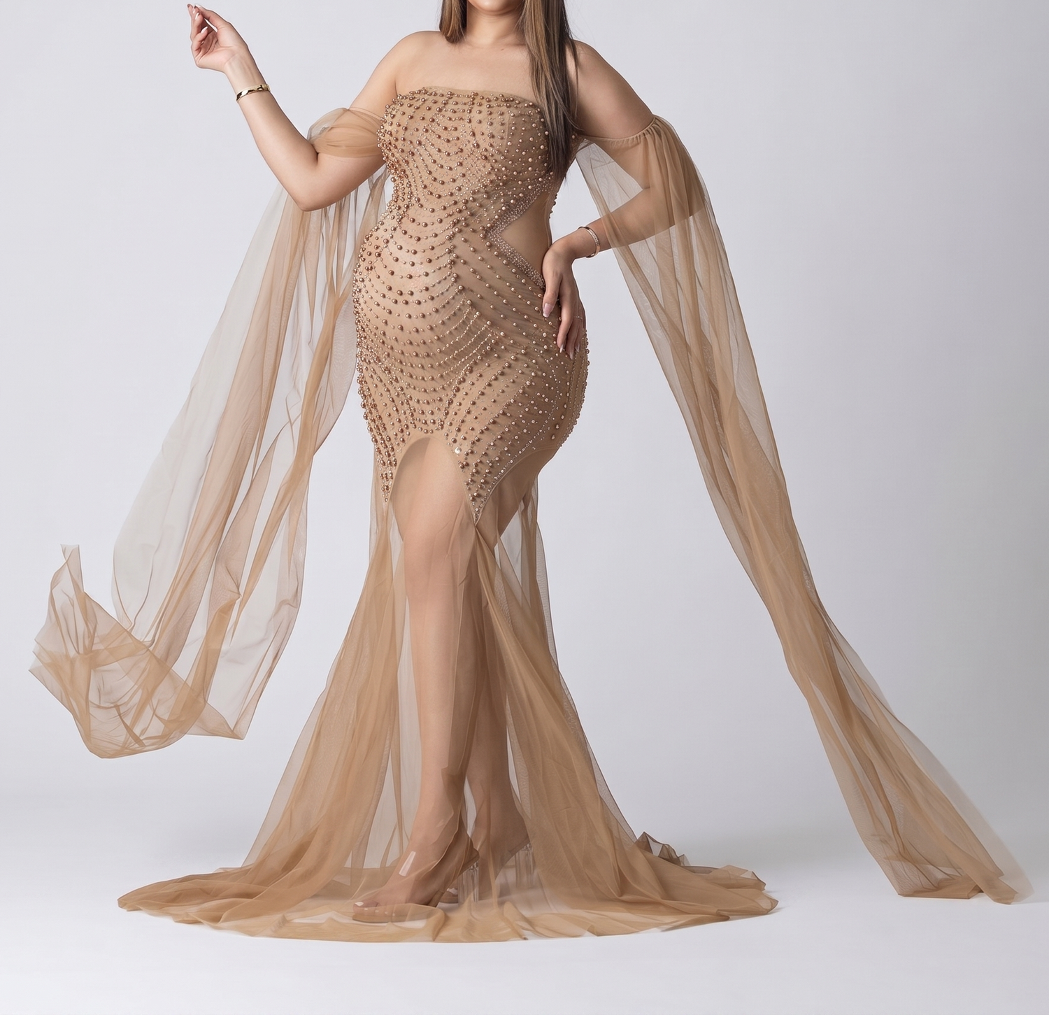 Woman wearing a stunning champagne gold beaded mesh gown with flowing sheer cape sleeves and a thigh-high slit.