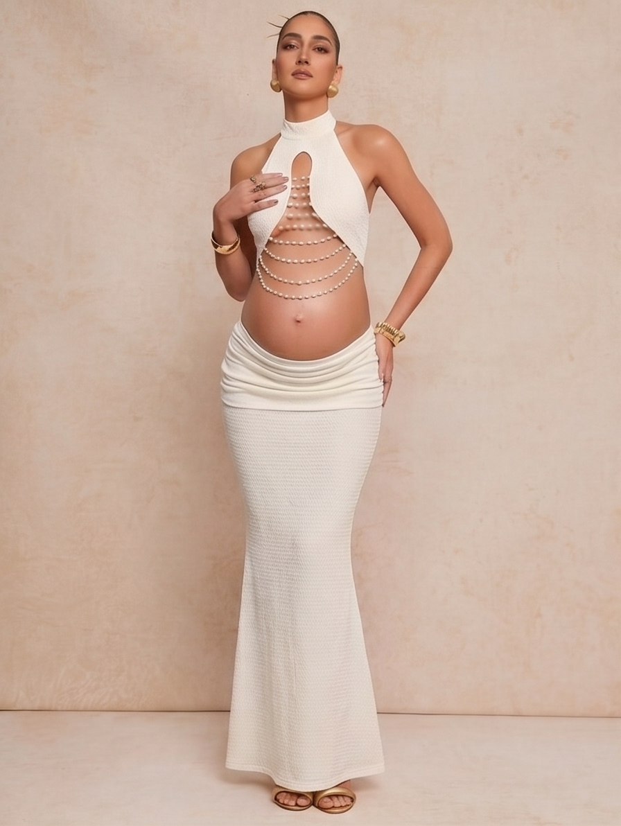 Pregnant woman in white halter maxi dress with chain detail cutout, showcasing a maternity-friendly elegant design.