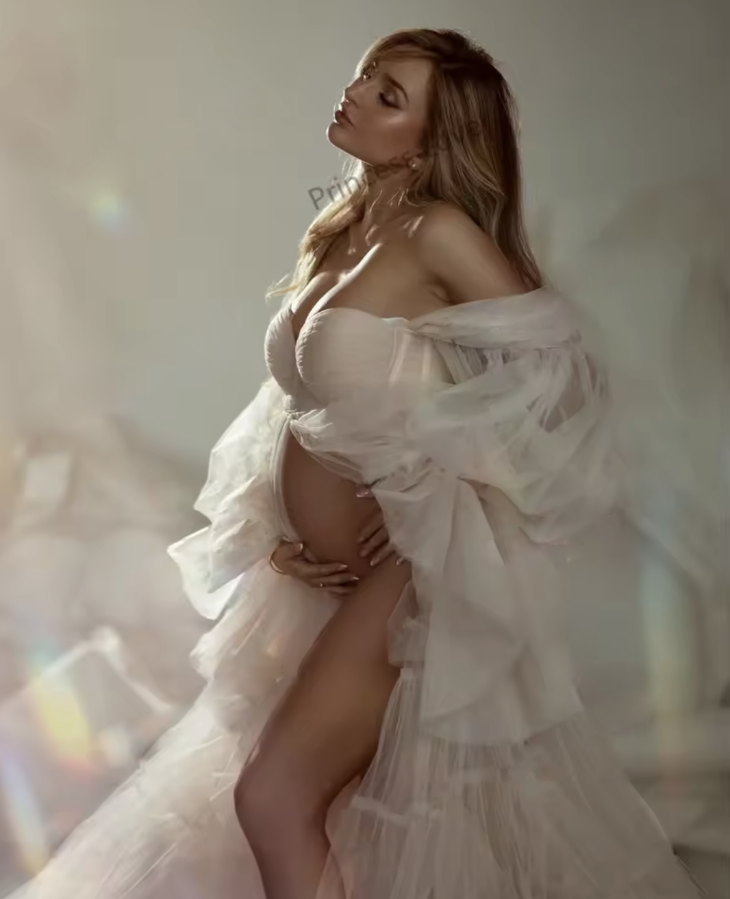 Pregnant woman in elegant white tulle off-shoulder gown posing gracefully in a soft, ethereal maternity photo shoot.