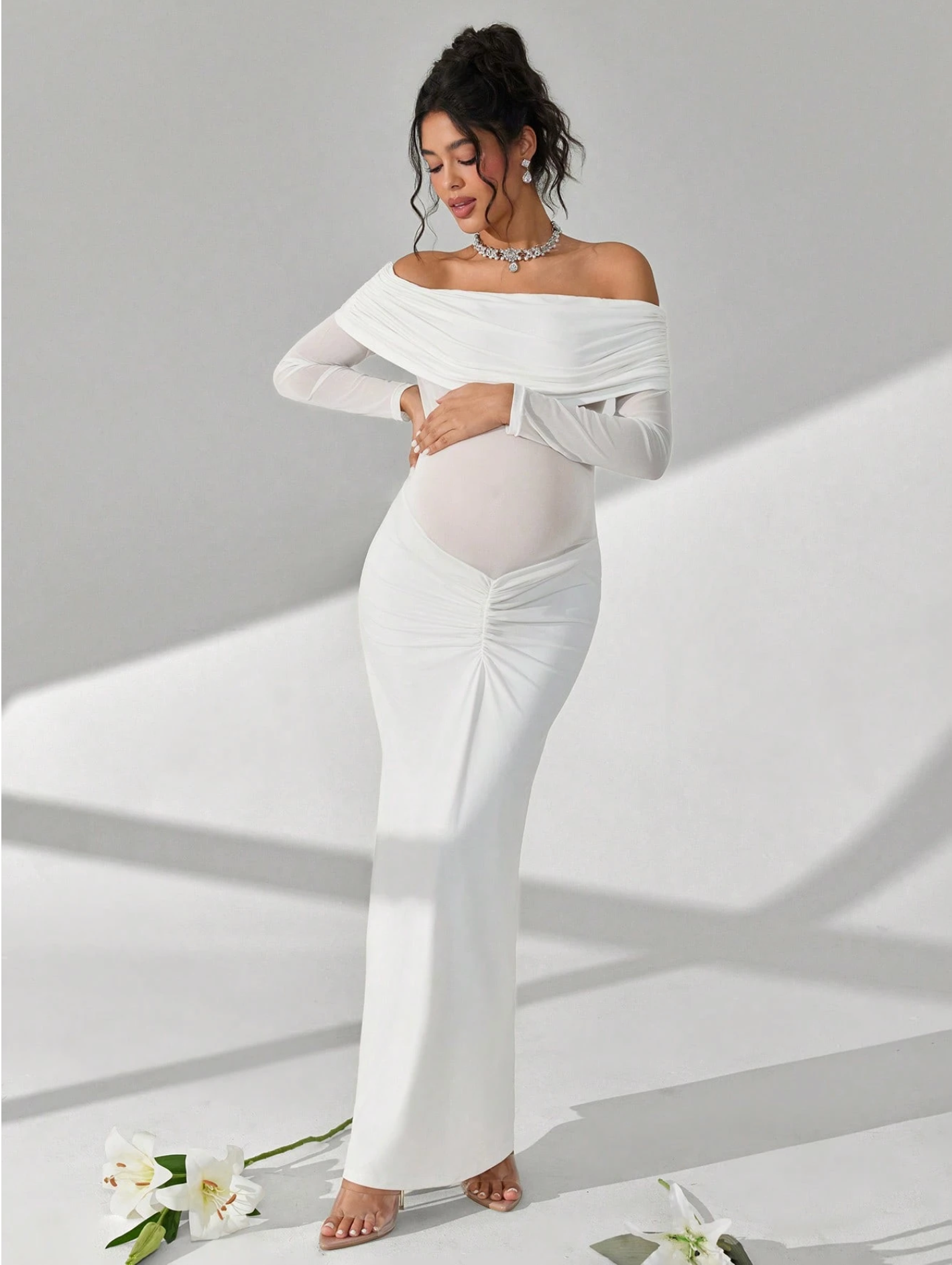 White off-shoulder long sleeve maternity maxi dress with sheer panel and ruched detail, shown on pregnant model.