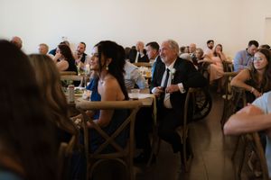 Wedding guests seated at tables in a bright venue, smiling and enjoying the reception celebration together.