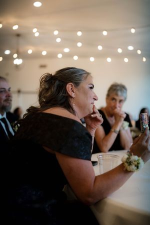 Emotional wedding guest wipes tear while watching ceremony inside decorated reception venue.