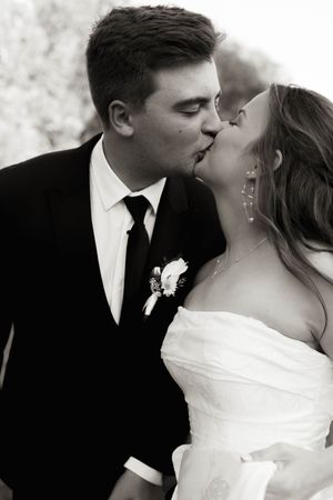 Black and white photo of bride and groom sharing a kiss, groom in black suit with floral boutonniere.