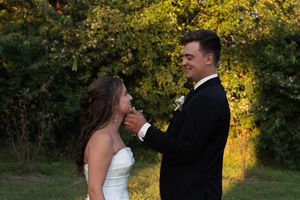Bride and groom sharing a joyful moment outdoors, with lush green trees in the background during golden hour.