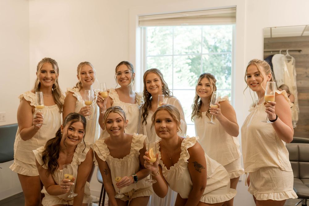 Group of bridesmaids in matching white ruffle outfits toasting with champagne glasses before a wedding celebration.