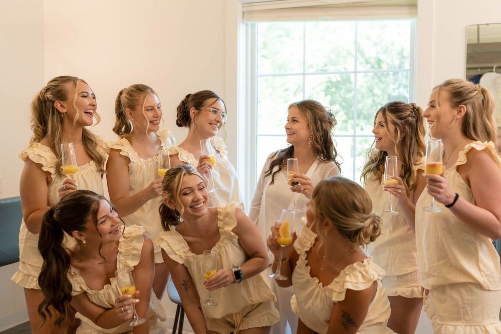 Bridesmaids in matching cream ruffled outfits laughing and holding champagne glasses during a bridal party getting ready.