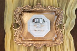 Wedding rings displayed in a white octagonal velvet ring box inside an ornate gold vintage frame.