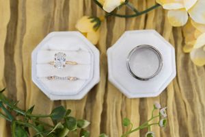 Elegant octagonal white velvet ring box displaying a diamond engagement ring and wedding band on a floral background.