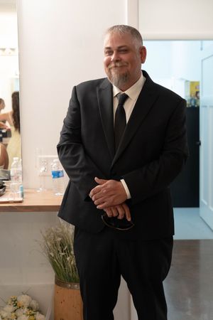 Man in black suit and tie with gray beard smiling at formal event.