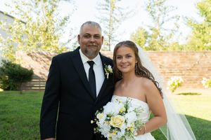 Smiling bride and groom pose together outdoors, bride holding white and yellow bouquet.