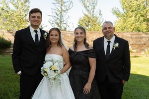 Wedding family portrait with bride, groom, and parents posing outdoors in formal attire.