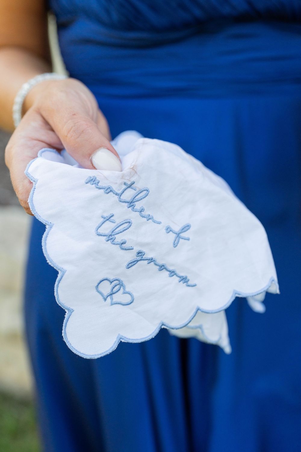 White handkerchief embroidered with blue cursive text reading mother of the groom with heart designs.