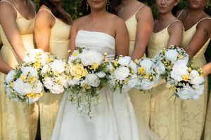 Bride in white gown with bridesmaids in yellow dresses holding white and yellow bouquets.