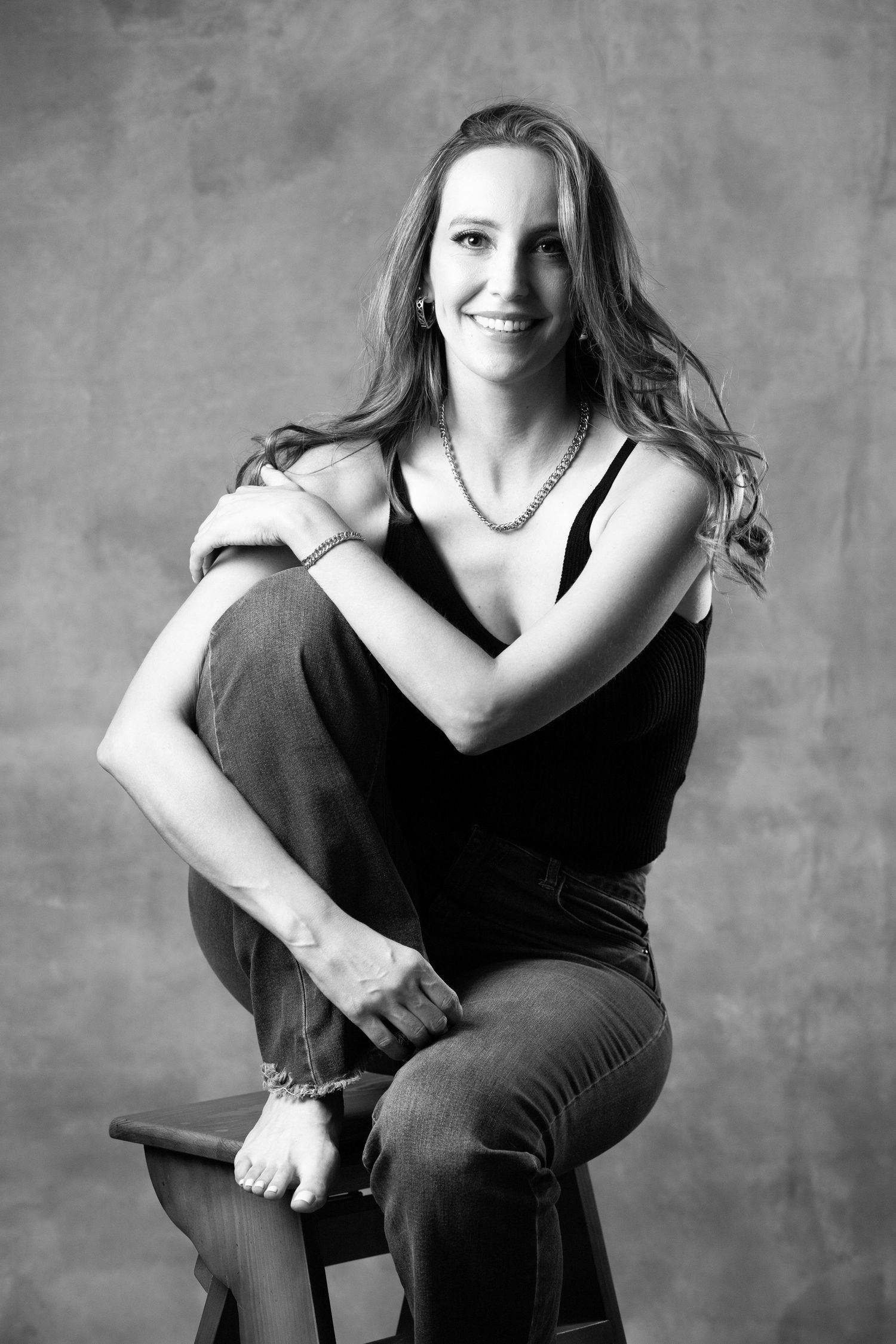 Black and white portrait in casual attire seated on wooden stool.
