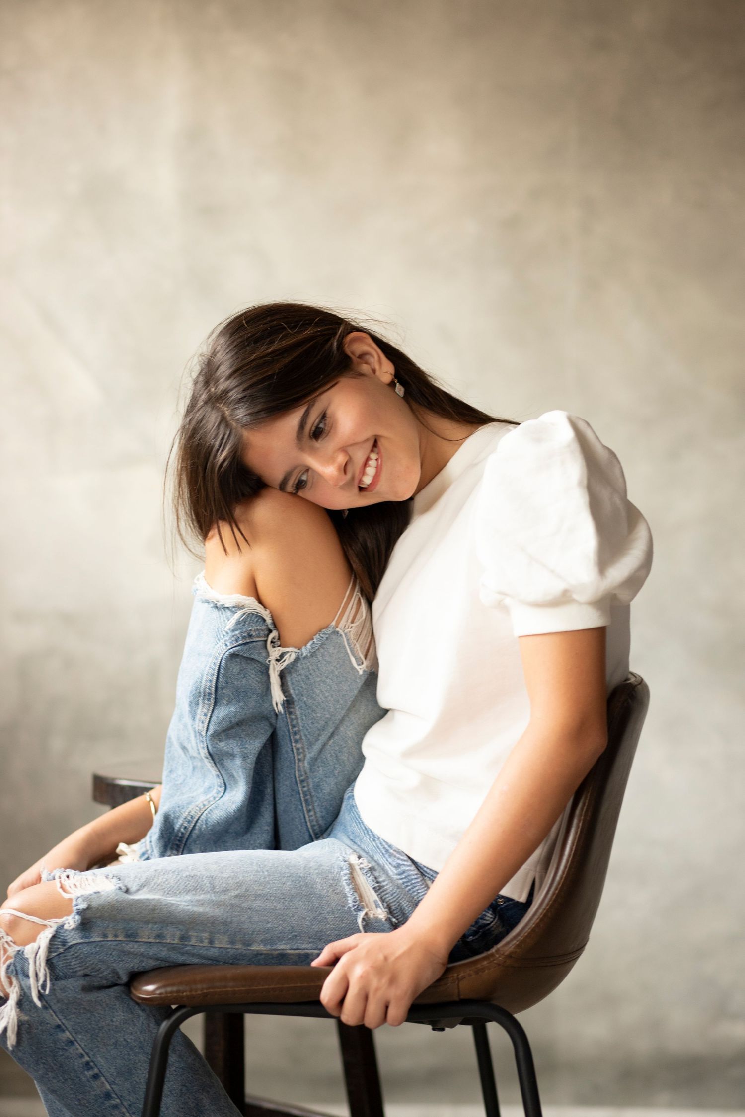 Portrait of a casual look featuring a white t-shirt and distressed jeans while seated on a wooden chair.