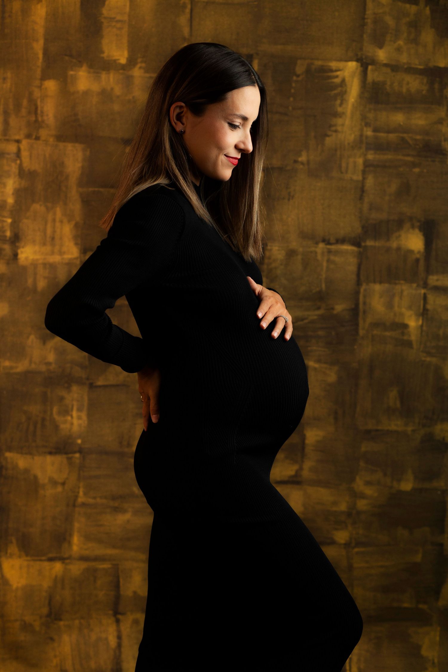 Silhouette of an expectant mother in a black dress against a golden textured background.