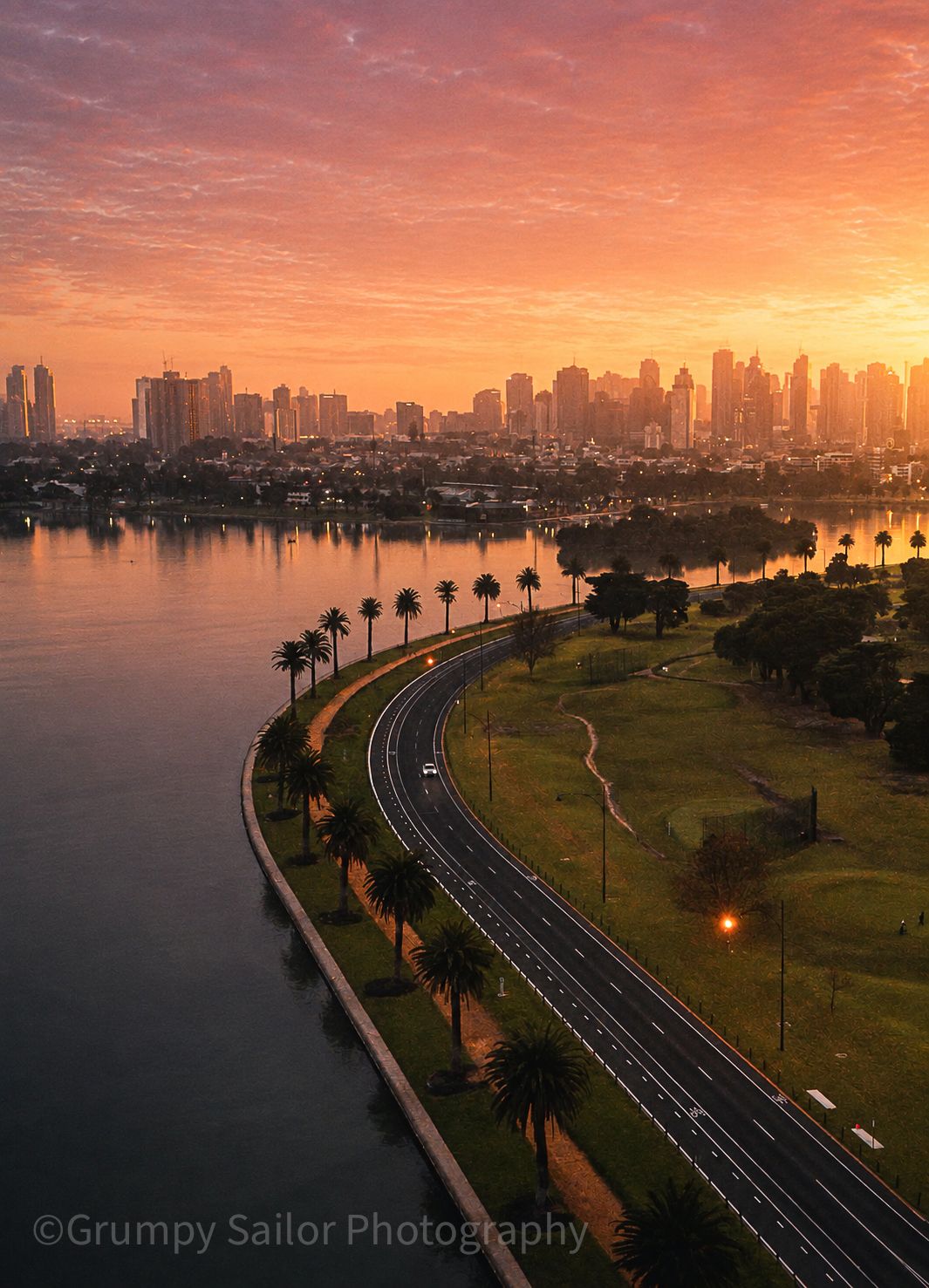 Stunning orange sunset over Melbourne city skyline with palm-lined waterfront road.