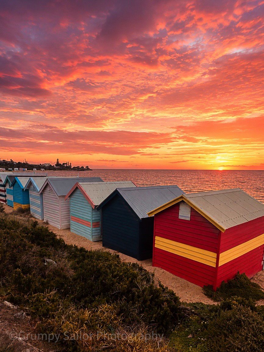 Colorful Brighton beach bathing boxes at sunrise under vivid red and orange sky.