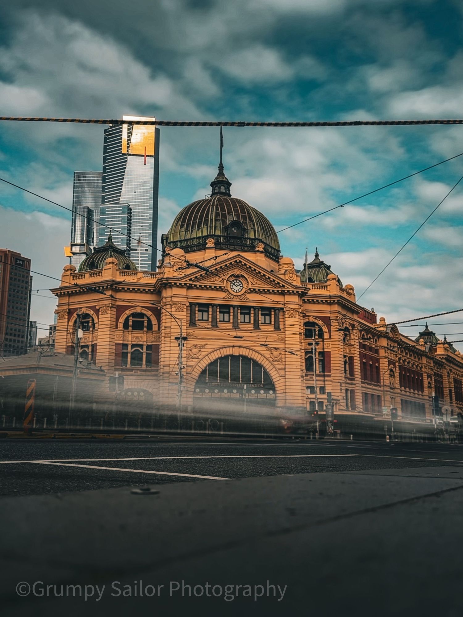 Flinders Street Station Melbourne with motion-blurred tram under dramatic cloudy sky.