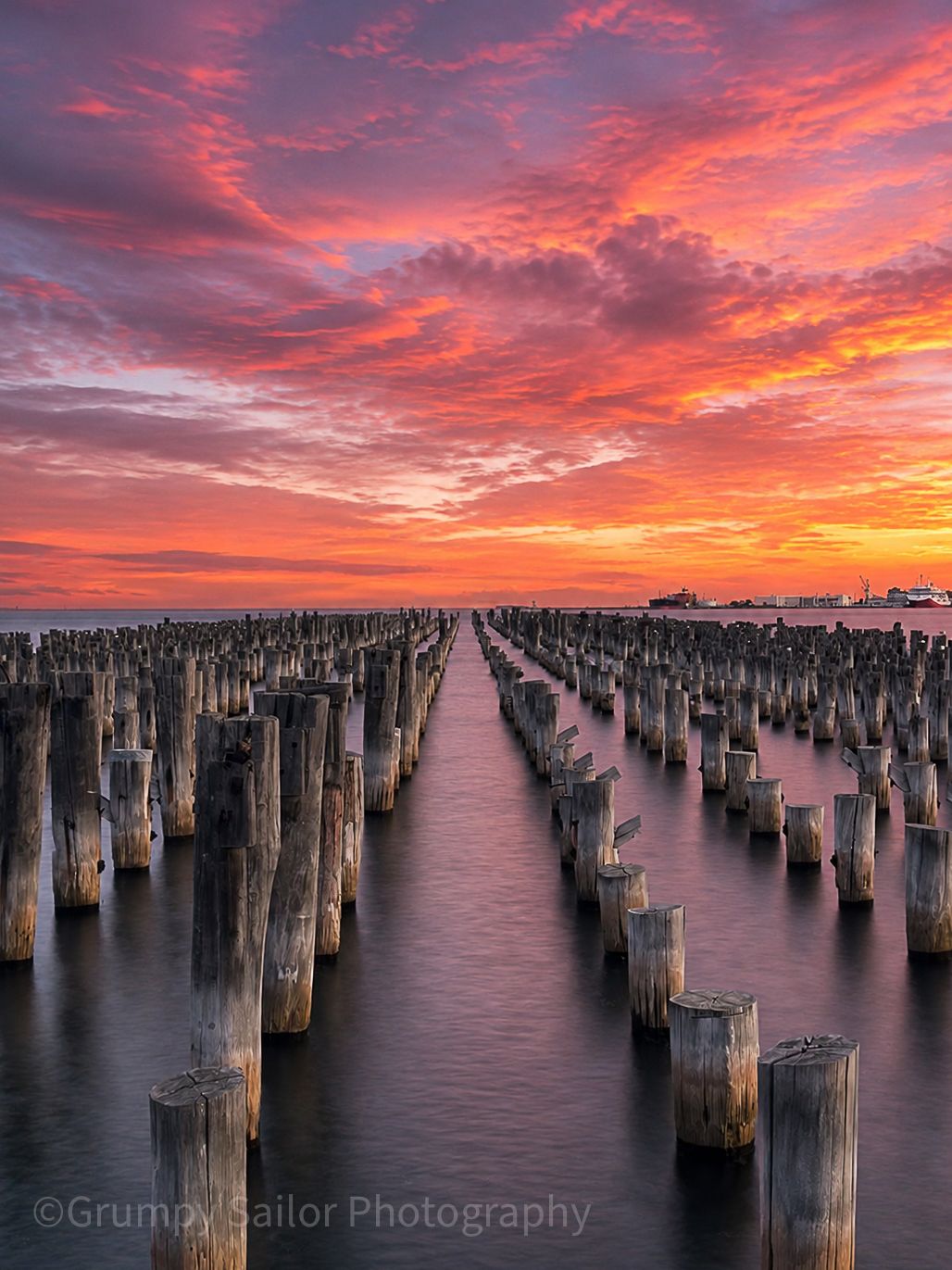 Dramatic red sunset sky over rows of historic wooden pylons at Princes Pier Melbourne.