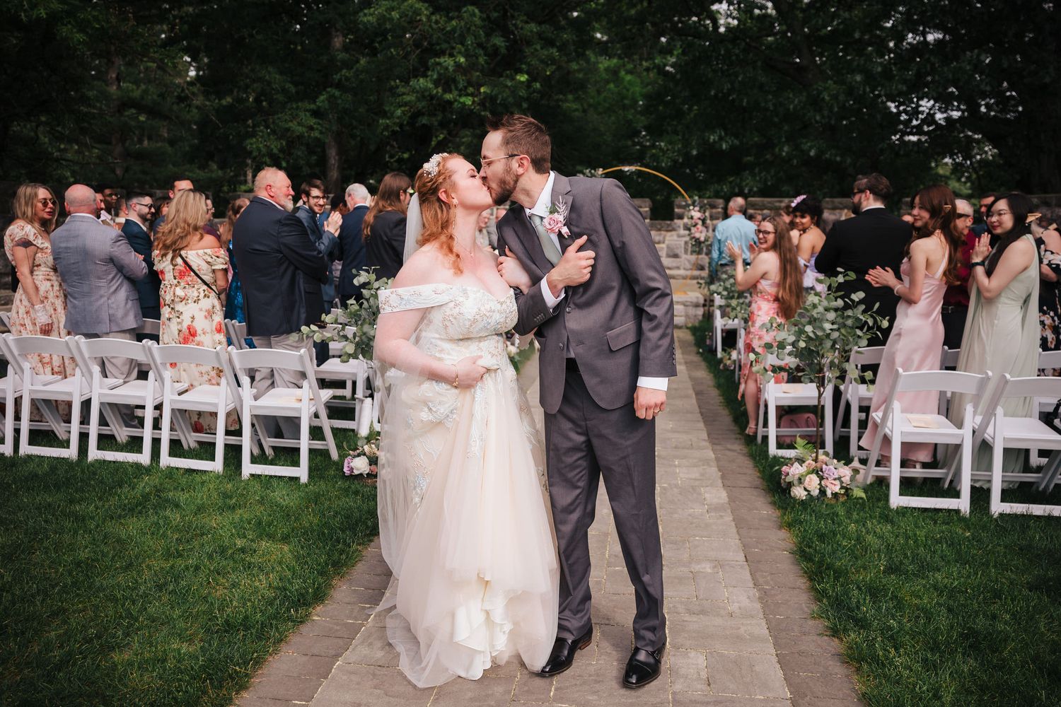 Newlyweds kissing while walking down the aisle as cheering guests clap on both sides after the ceremony.