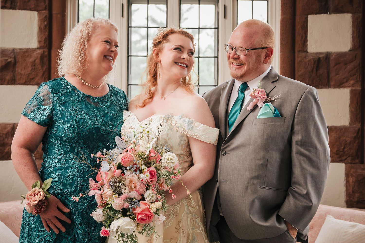 Bride laughing with her mother and father in a sunroom with arched stone windows at Searles Castle.