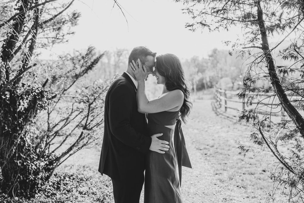 Black and white photo of a couple sharing a romantic kiss outdoors among trees.