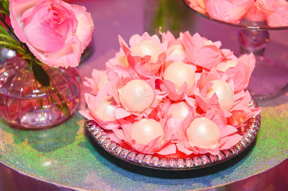 Pink rose petals and white pearl balls arranged elegantly on a decorative silver plate beside a pink rose vase centerpiece.