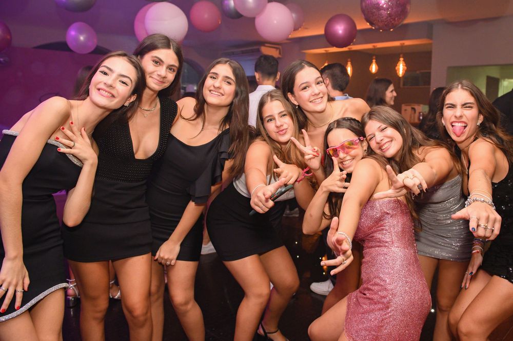 Group of young women posing together at a party with balloons and purple lighting in the background.