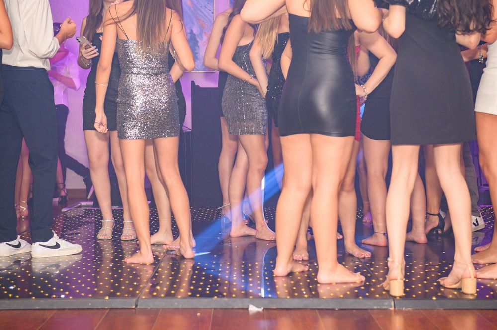 Group of young women dancing in short dresses on a illuminated dance floor at a nightclub party.