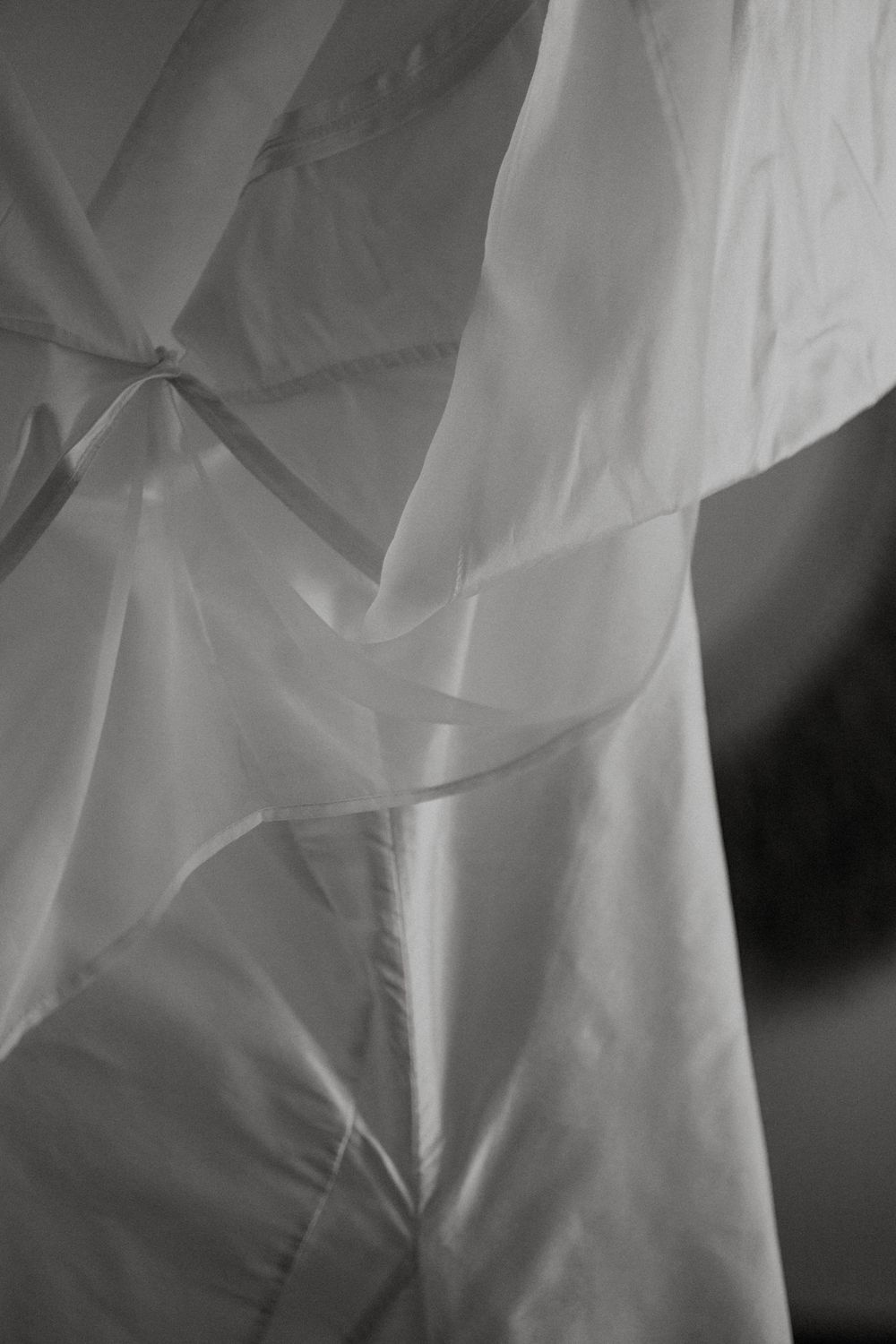 Black and white close-up of flowing white fabric with soft folds and delicate translucent layers creating elegant texture.