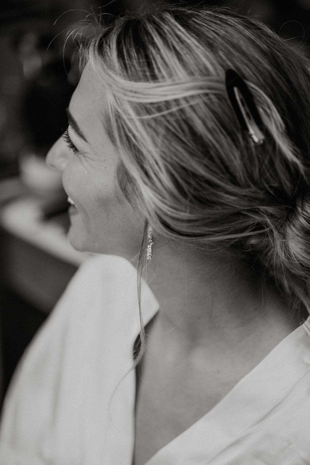 Black and white profile portrait of a smiling woman with updo hairstyle wearing elegant drop earrings and white top.