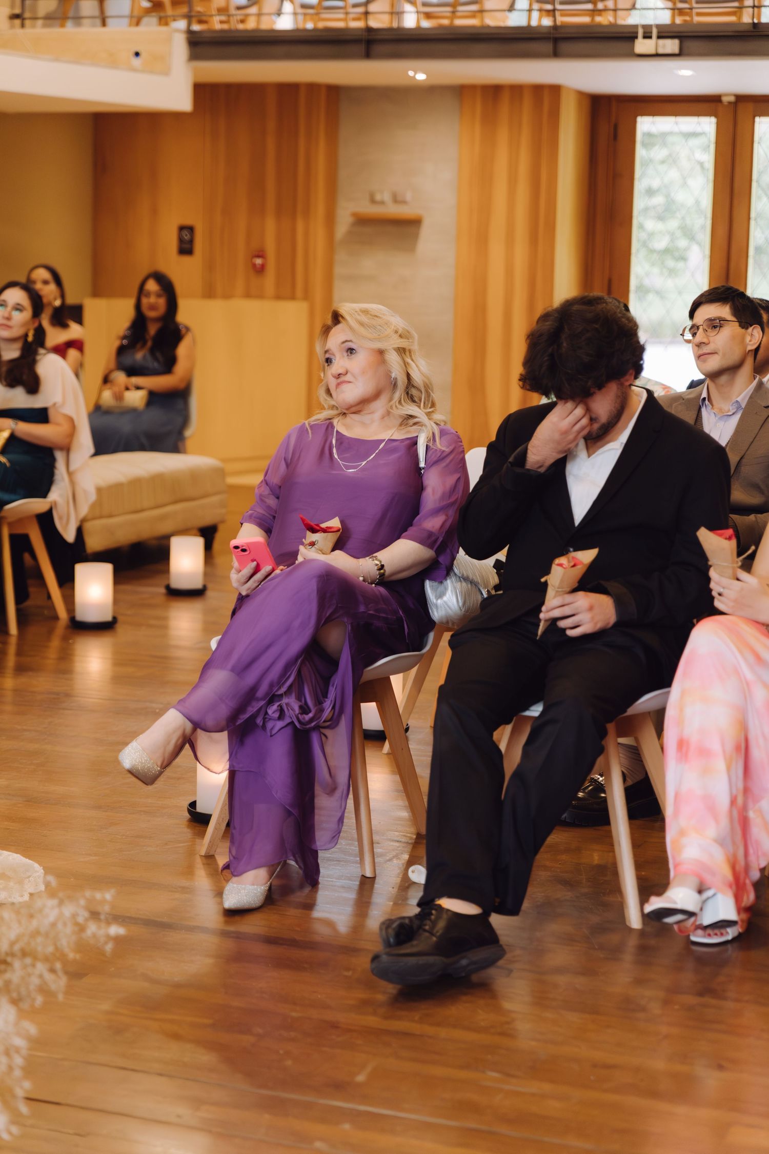 Emotional wedding guest in purple dress wiping tears during ceremony with candles nearby.