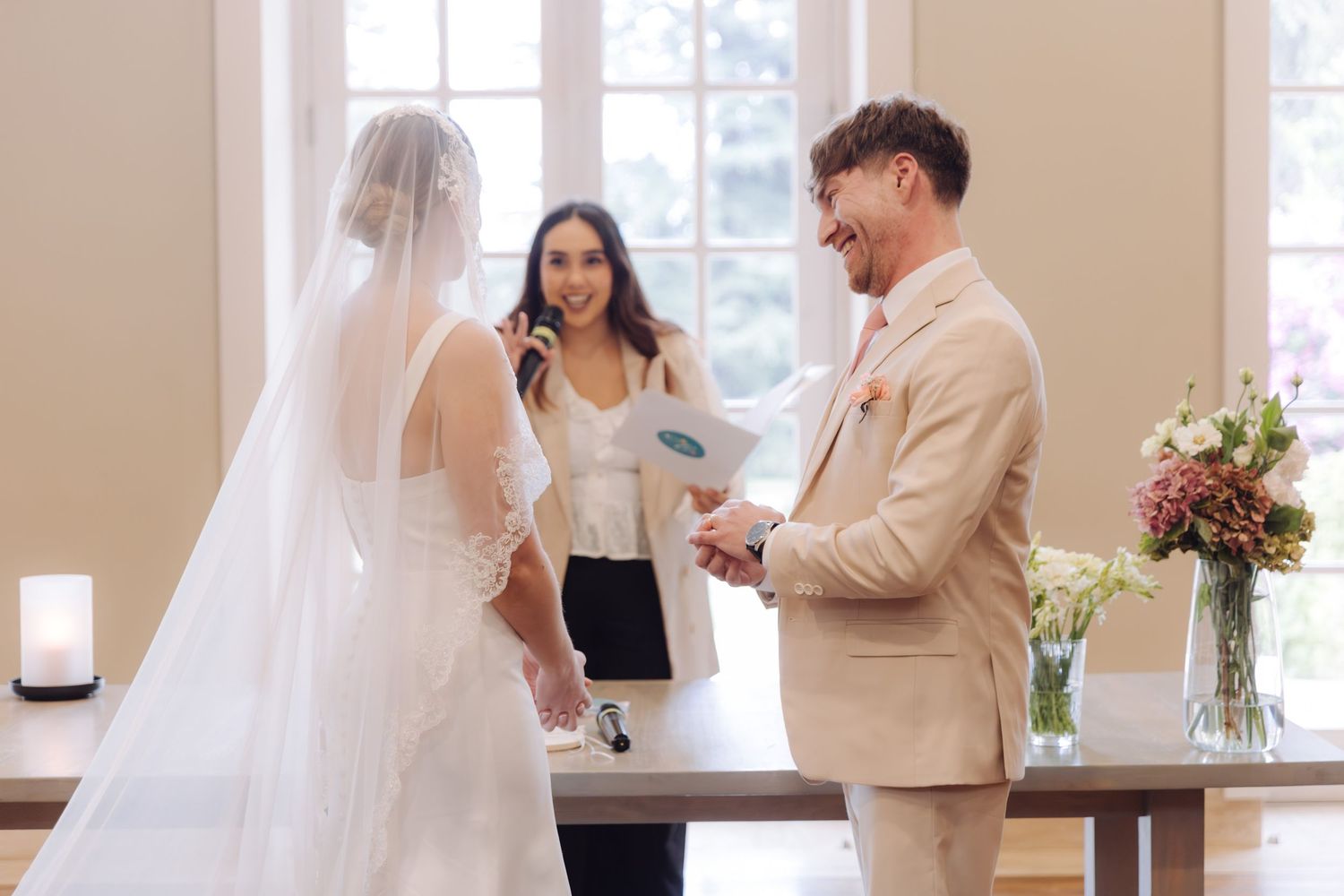 Groom reads vows to bride while officiant smiles during elegant wedding ceremony.