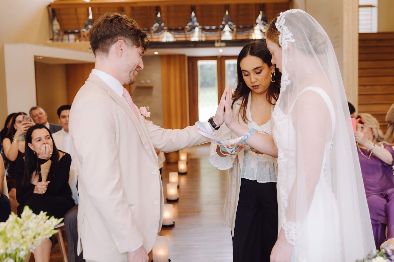 Officiant ties hands of bride and groom during wedding ring exchange ceremony.