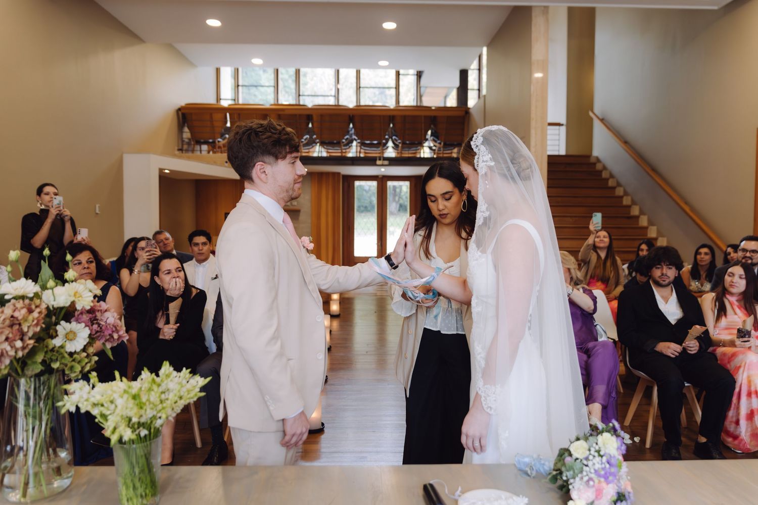 Bride and groom hold hands during wedding ceremony with guests seated in background.